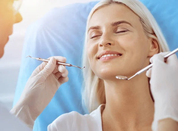 在阳光灿烂的牙科诊所接受牙医检查的金发女人笑着。健康的牙齿和医学概念 — 图库照片