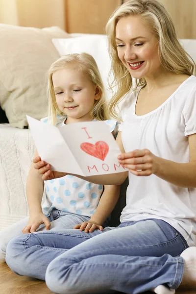 Bonne fête des mères dans un appartement ensoleillé. Enfant fille félicite maman et donne sa carte postale avec le dessin du cœur. Concept de famille — Photo
