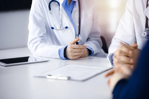 Dois médicos e uma paciente discutindo algo enquanto estavam sentados na mesa da clínica moderna. Serviço médico perfeito, conceito de medicina — Fotografia de Stock