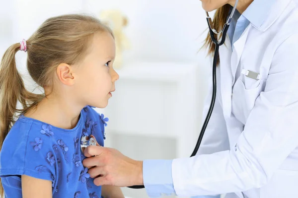 Arzt untersucht ein kleines Mädchen per Stethoskop. Glücklich lächelnder Kinderpatient bei der üblichen ärztlichen Untersuchung. Medizin- und Gesundheitskonzepte — Stockfoto