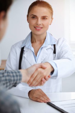 Kadın doktor, erkek hastasıyla tokalaşırken gülümsüyor. Tıp konsepti