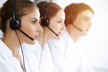 Merkezi ara. Güzel genç bir kadın güneşli ofisteki müşterilere yardım etmek için kulaklık ve bilgisayar kullanıyor. İş konsepti