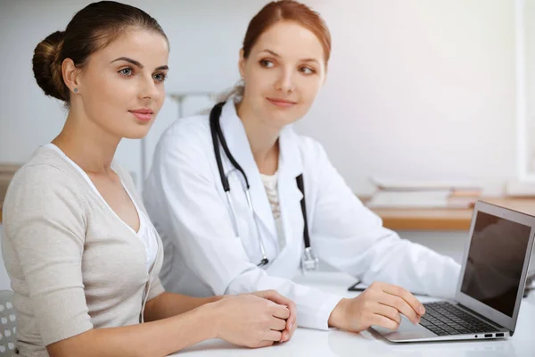 Médico e paciente estão sentados e discutindo os resultados do exame de saúde ao usar o computador portátil. Saúde, medicina e boas notícias conceitos — Fotografia de Stock