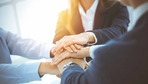 Business team showing unity with their hands together in sunny office. Group of people joining hands and representing concept of friendship, teamwork and partnership