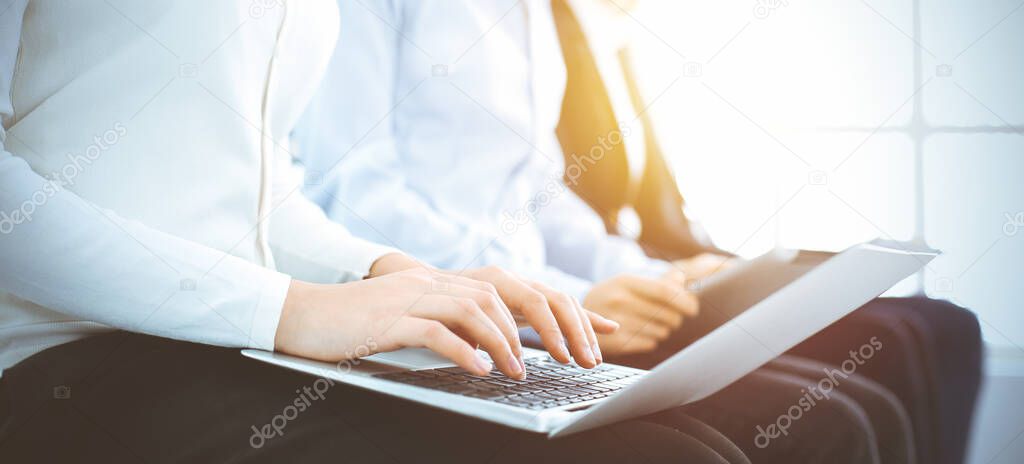 Group of diverse business people working in sunny office, close-up. Woman typing on laptop computer. Conference or training concepts
