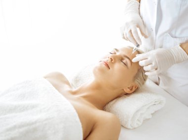 Güzellik uzmanı elleri güneşli klinikte kadın yüzüne şırınga ile güzellik prosedürü uyguluyor. Kozmetik tıp ve cerrahi, güzellik enjeksiyonları konsepti