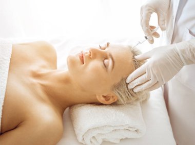 Güzellik uzmanı elleri güneşli klinikte kadın yüzüne şırınga ile güzellik prosedürü uyguluyor. Kozmetik tıp ve cerrahi, güzellik enjeksiyonları konsepti