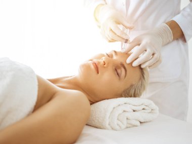 Güzellik uzmanı elleri güneşli klinikte kadın yüzüne şırınga ile güzellik prosedürü uyguluyor. Kozmetik tıp ve cerrahi, güzellik enjeksiyonları konsepti