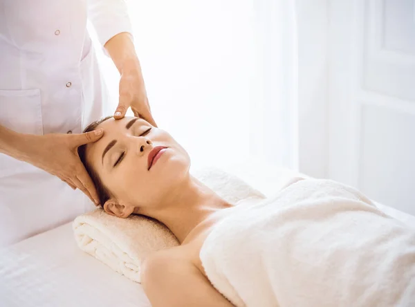 Hermosa mujer disfrutando de masaje facial con los ojos cerrados en el centro de spa soleado — Foto de Stock