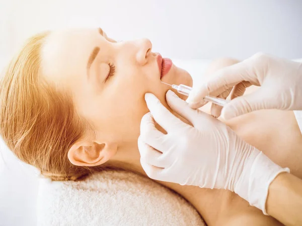 Beautiful woman receiving beauty injections with closed eyes in sunny medical center. Beautician doctor hands doing beauty procedure to female face with syringe. Cosmetic medicine and surgery concept — Stock Photo, Image