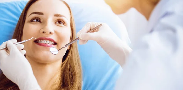 在阳光灿烂的牙科诊所接受牙医检查的带着正牙托的年轻女子的微笑。健康的牙齿和医学概念 — 图库照片