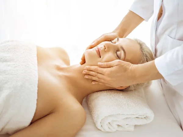 Mulher loira bonita desfrutando de massagem facial com olhos fechados no centro de spa ensolarado. Tratamento relaxante em medicina e conceitos de beleza — Fotografia de Stock