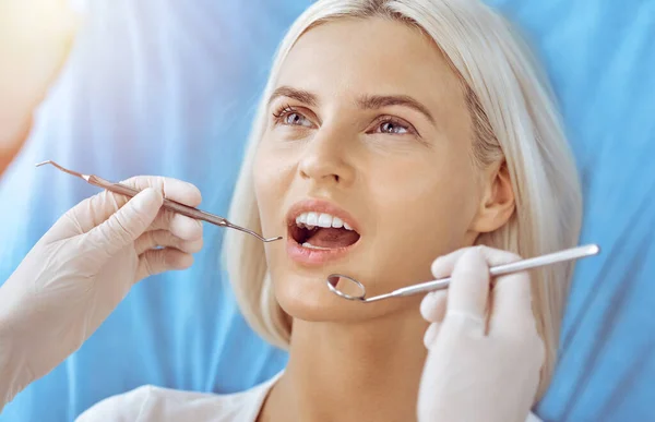 Uśmiechnięta blondynka badana przez dentystę w słonecznej klinice dentystycznej. Zdrowe zęby i koncepcja medycyny — Zdjęcie stockowe