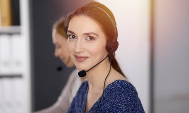 Latin Amerikalı iş kadını güneşli bir ofiste otururken kulaklıkla konuşuyor. Çağrı merkezi ve çeşitli iş grupları