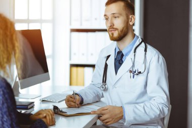 Dost canlısı kızıl sakallı doktor ve hasta kadın güneşli klinikte otururken sağlık muayenesini tartışıyorlar. Tıp konsepti