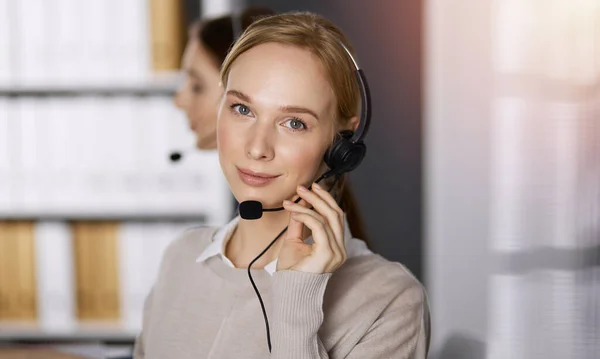 Mujer de negocios hablando con auriculares mientras está sentada en una oficina soleada. Centro de llamadas y grupo de personas diversas en los negocios — Foto de Stock