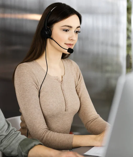 Deux jeunes dans des casques d'écoute parlent aux clients, assis au bureau dans un bureau moderne. Concentre-toi sur la femme. Opérateurs de centre d'appels au travail — Photo