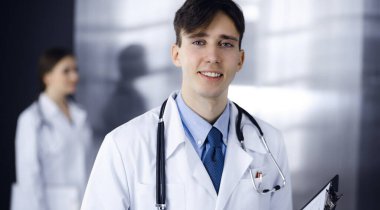 Modern klinikte dostane genç bir erkek doktor elinde bir panoyla dikiliyor. Bayan meslektaşım, doktorların arka planında ilaç kayıtları doldurmakla meşgul. Tıp konsepti