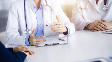Erkek meslektaşı olan bilinmeyen kadın-doktor güneşli klinikteki masada otururken hastaya danışıyor, yakın plan. Covid 2019