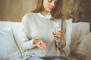 Yakın plan kadın hapları tutuyor, ilaç alıyor, baş ağrısını tedavi ediyor, yüksek tansiyon ilaçları evde. Coronavirus salgını sırasında evde konsept kal