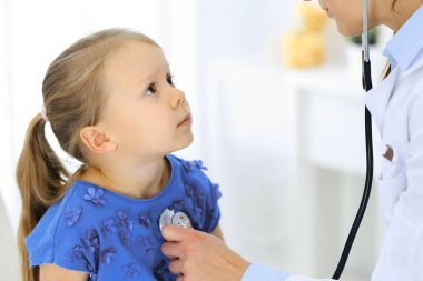 Doktor steteskopla küçük bir kızı muayene ediyor. Her zamanki tıbbi muayenede gülümseyen çocuk hasta. Tıp ve sağlık hizmetleri kavramları
