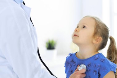 Doktor steteskopla küçük bir kızı muayene ediyor. Her zamanki tıbbi muayenede gülümseyen çocuk hasta. Tıp ve sağlık hizmetleri kavramları