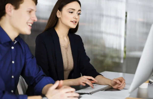 Jóvenes empresarios amigables en el trabajo, mientras se sientan juntos en el escritorio en un gabinete. Concéntrate en mujer. Retrato en la cabeza o de negocios en una oficina moderna — Foto de Stock