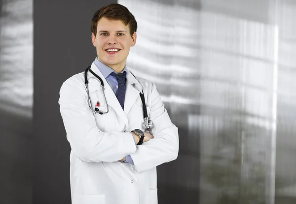 Alegre joven médico está de pie con los brazos cruzados en una clínica. Retrato de médico profesional en el trabajo. Concepto de medicina — Foto de Stock