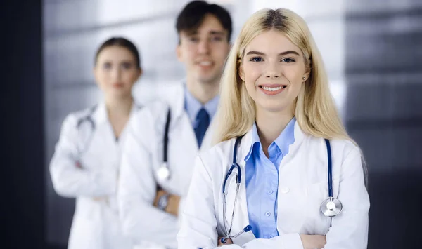 Gruppo di tre giovani medici in piedi come una squadra con le braccia incrociate in clinica moderna e pronto ad aiutare i pazienti. Concetto di medicina — Foto Stock