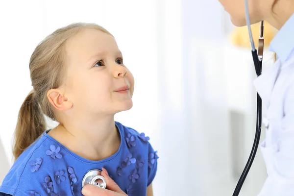 医生用听诊器检查一个小女孩.在通常的医疗检查中快乐地微笑着的儿童病人。医药和保健概念 — 图库照片