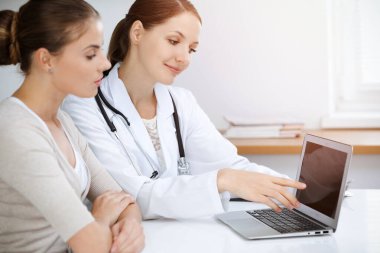 Doktor ve hasta dizüstü bilgisayar kullanırken sağlık muayenesi sonuçlarını tartışıyor.