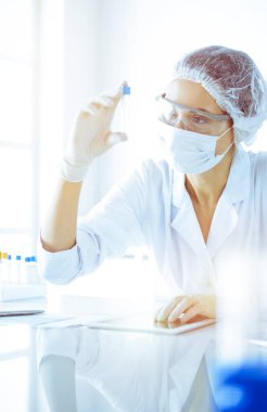 Koruyucu gözlüklü profesyonel kadın bilim adamı güneşli laboratuarda mavi tonda reaksiyonlarla araştırma tüpü kullanıyor. Tıp ve bilim araştırmaları