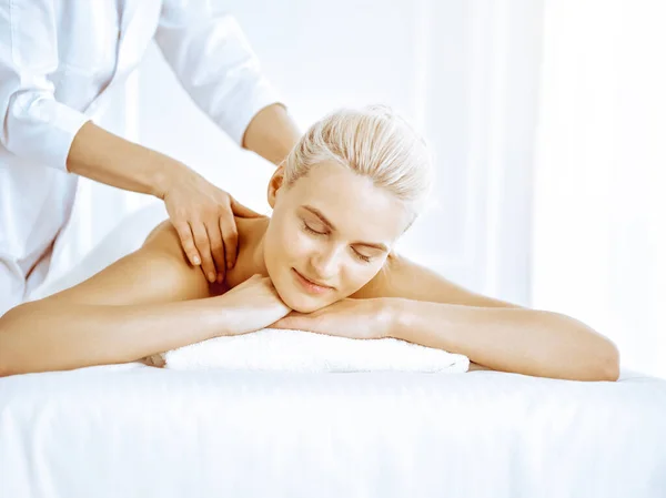Beautiful blonde woman enjoying back massage in spa center. Beauty and lifestyle