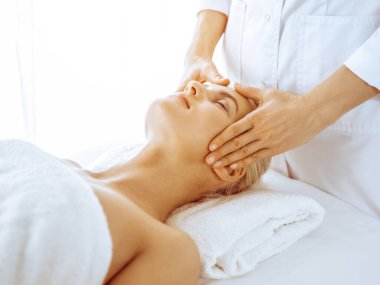 Güzeller güzeli sarışın kadın spa merkezinde yüz masajından hoşlanıyor. Tıp ve güzellik kavramlarında rahatlatıcı tedavi