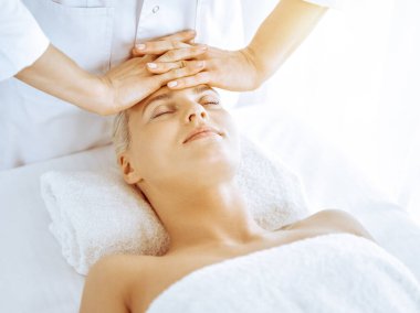 Güzeller güzeli sarışın kadın spa merkezinde yüz masajından hoşlanıyor. Tıp ve güzellik kavramlarında rahatlatıcı tedavi