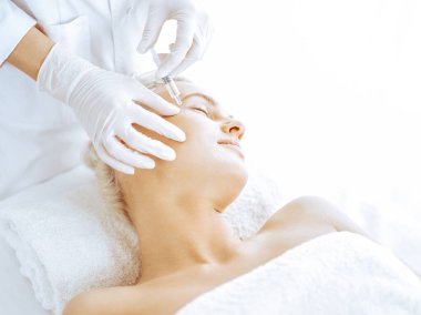 Güzellik uzmanı elleri klinikte şırıngalı kadın sarışına güzellik prosedürü uyguluyor. Kozmetik tıp ve cerrahi, güzellik enjeksiyonları konsepti