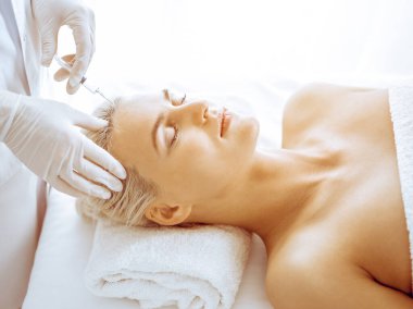 Güzellik uzmanı elleri klinikte şırıngalı kadın sarışına güzellik prosedürü uyguluyor. Kozmetik tıp ve cerrahi, güzellik enjeksiyonları konsepti