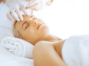 Güzellik uzmanı elleri klinikte şırıngalı kadın sarışına güzellik prosedürü uyguluyor. Kozmetik tıp ve cerrahi, güzellik enjeksiyonları konsepti