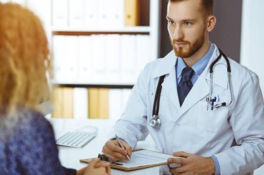 Dost canlısı kızıl sakallı doktor ve hasta kadın güneşli klinikte otururken sağlık muayenesini tartışıyorlar. Tıp konsepti