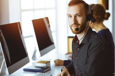 Günümüz güneşli ofisinde otururken, kulaklıkla konuşan kızıl sakallı bir iş adamı. Çağrı merkezinde çeşitli insanlar grubu