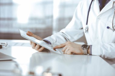 Bilinmeyen erkek doktor klinikteki tablet bilgisayarla yakın planda çalışıyor. İşteki genç doktor. Mükemmel sağlık hizmeti, tıp konsepti