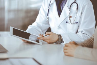 Bilinmeyen erkek doktor ve hasta kadın klinikte oturup tablet bilgisayar kullanırken bir şeyler tartışıyorlar. Hastanedeki en iyi sağlık hizmeti, ilaç, salgın durdurma.