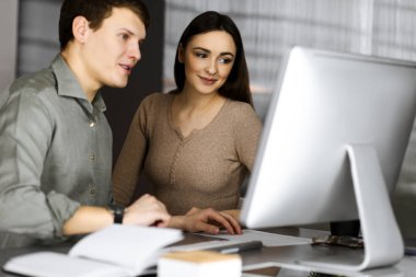 Yeşil gömlekli arkadaş canlısı genç işadamı ve programcı, modern bir ofiste masa başında bayan bir meslektaşla birlikte otururken bilgisayar üzerinde çalışıyor. Kadınlara odaklan. Başarılı olma kavramı