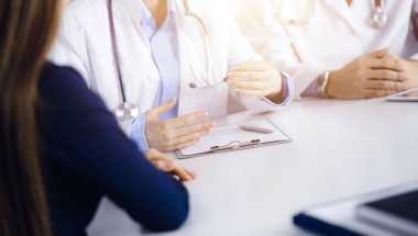 Erkek meslektaşı olan bilinmeyen kadın-doktor güneşli klinikteki masada otururken hastaya danışıyor, yakın plan. Covid 2019