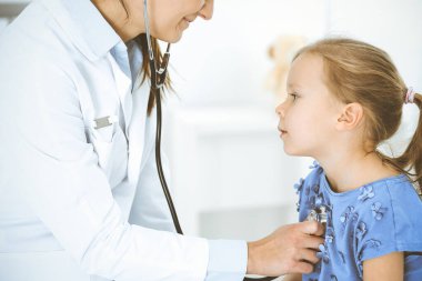 Doktor steteskopla küçük bir kızı muayene ediyor. Her zamanki tıbbi muayenede gülümseyen çocuk hasta. Tıp ve sağlık hizmetleri kavramları