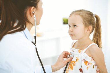 Doktor steteskopla küçük bir kızı muayene ediyor. Her zamanki tıbbi muayenede gülümseyen çocuk hasta. Tıp ve sağlık hizmetleri kavramları