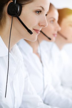 Merkezi ara. Güzel genç bir kadın güneşli ofisteki müşterilere yardım etmek için kulaklık ve bilgisayar kullanıyor. İş konsepti