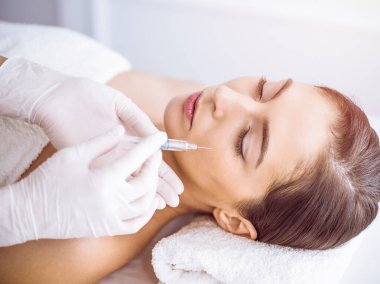 Güzellik uzmanı güneşli spa merkezinde genç esmer bir kadının yüzüne şırıngayla güzellik prosedürü uyguluyor. Kozmetik ilaç ve ameliyat, güzellik iğneleri.