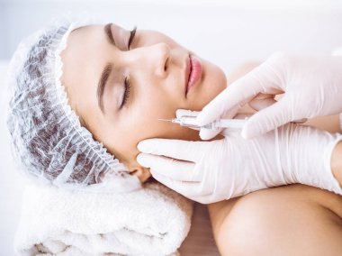 Güzellik uzmanı güneşli spa merkezinde genç esmer bir kadının yüzüne şırıngayla güzellik prosedürü uyguluyor. Kozmetik ilaç ve ameliyat, güzellik iğneleri.