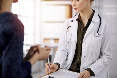 Neşeli gülümseyen kadın doktor ve hasta kadın güncel sağlık muayenesini güneşli klinikte otururken tartışıyorlar. Hastanede mükemmel bir tıbbi hizmet. Tıp konsepti